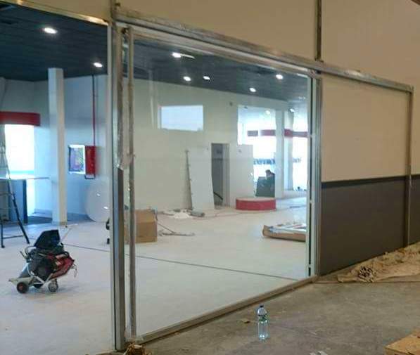 Puerta corredera de acero inoxidable y vidrio para acceso de vehículos en concesionario. Puerta corredera de acero inoxidable y vidrio para acceso de vehículos en concesionario.