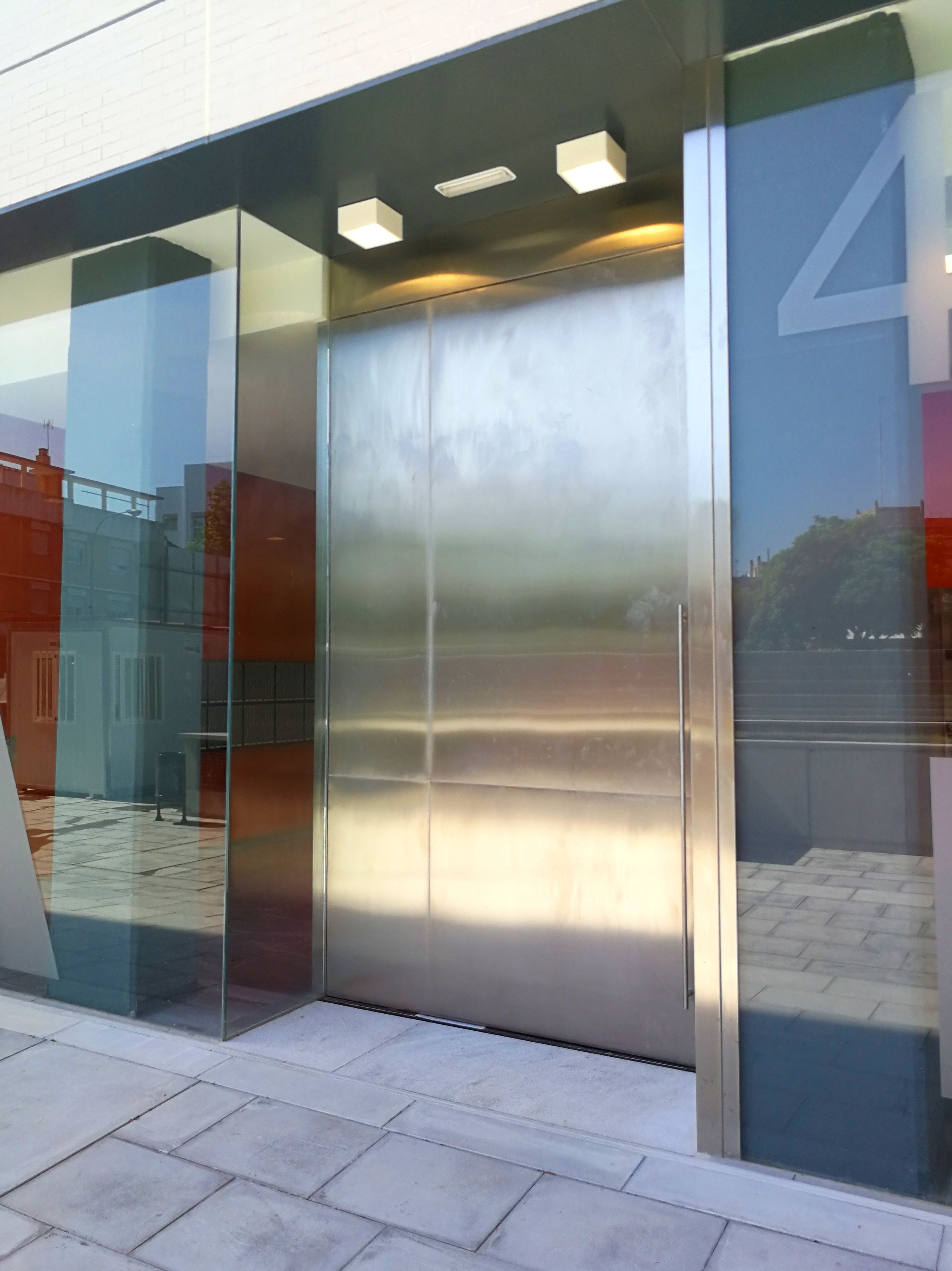 Puerta de acero inoxidable con diseño personalizado para edificio de comunidad de vecinos. Puerta de acero inoxidable con diseño personalizado para edificio de comunidad de vecinos.