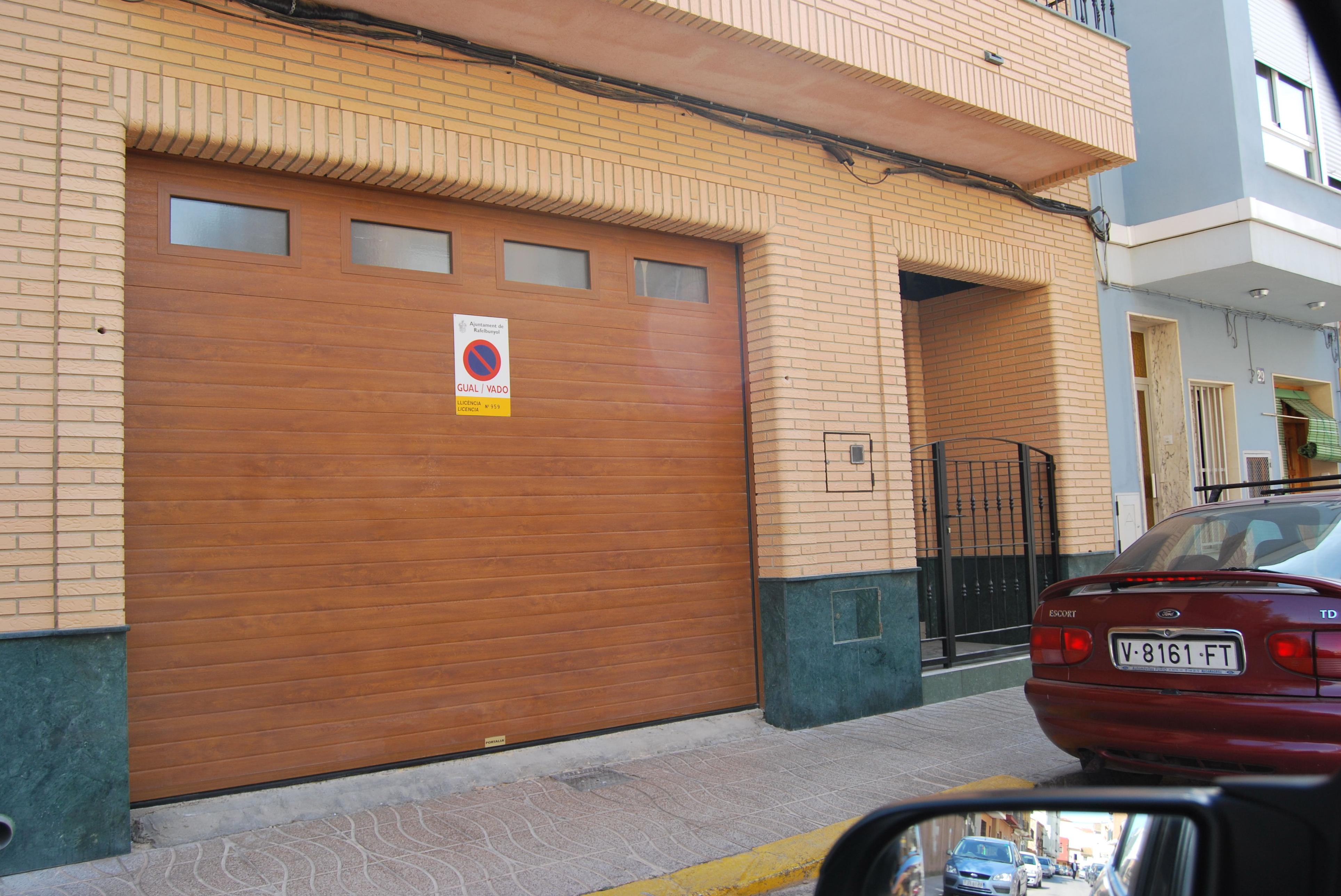 Puerta seccional de panel acanalado en color madera con fijos en el panel superior. Puerta seccional de panel acanalado en color madera con fijos en el panel superior.