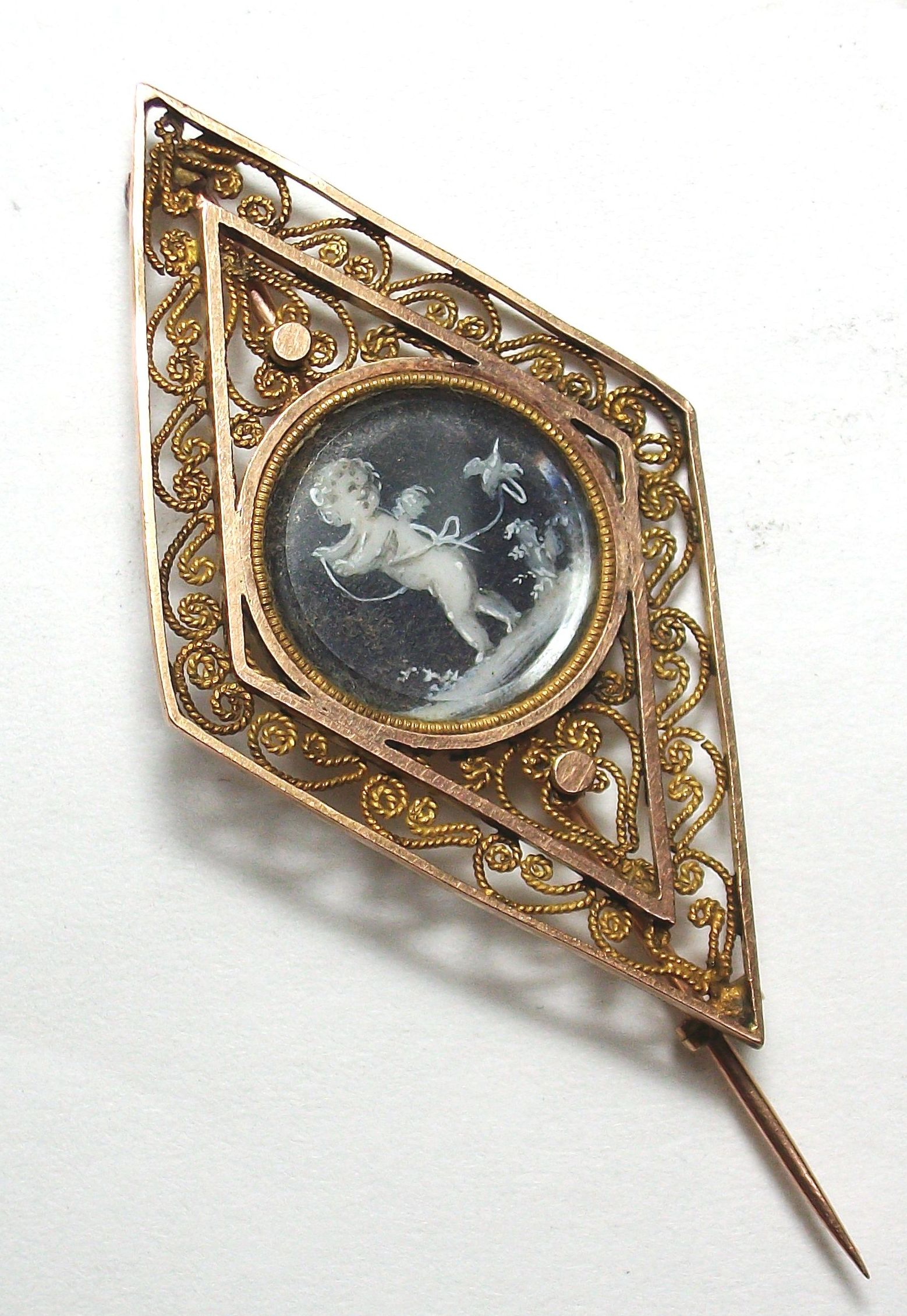 Broche romboidal realizado en oro de 18k  con filibrana y tondo central con putti pintado en acuarela. Principios s. XIX. VENDIDO